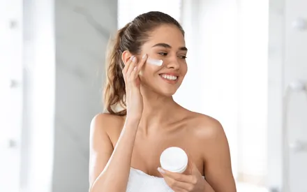 "Femme à la peau nette appliquant une crème hydratante ou un soin du visage, mettant en avant la texture onctueuse du produit.