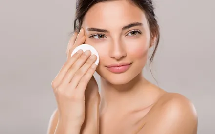Femme souriante utilisant le Démaquillant 2-en-1 Lait + Tonique, une émulsion légère qui nettoie et apaise la peau en un seul geste. Emulsion-démaquillante