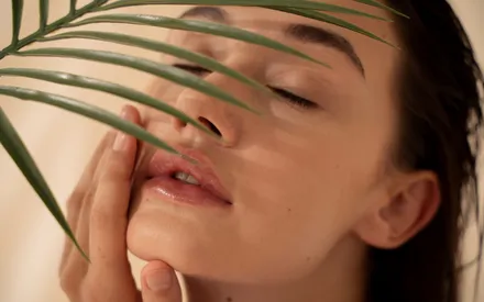 Jeune femme étalant la pâte gommante sur son visage. On aperçoit au premier plan une feuille de bambou qui cache légèrement une partie de son visage, pour rappeler la présence de poudre de bambou qui permet une exfoliation douce.