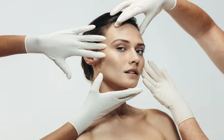 Gros plan d'une femme à la peau parfaite repoussant doucement une main gantée, symbolisant l'efficacité naturelle de la Crème tenseur flash anti-âge.