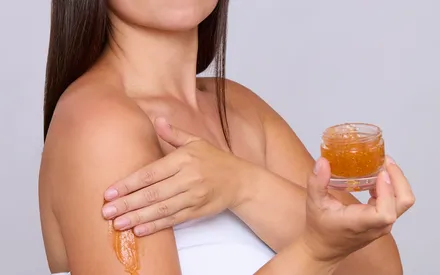 Une mannequin brune applique sur son bras le gommage datte-figue, un soin à la couleur orangée et profondément gourmand