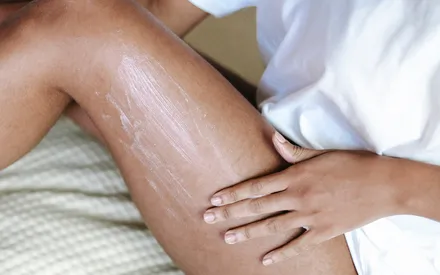 Cuisse d’une femme qui étale de la crème corps à la texture tendre, cette crème enveloppe la peau dans un soin réconfortant.