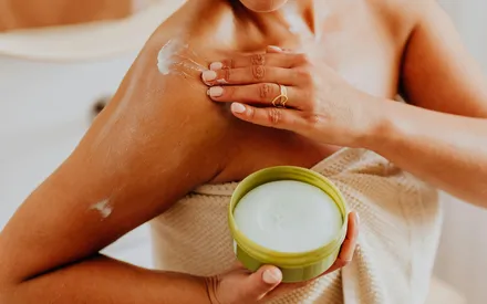 Femme qui s’étale du beurre hydratant sur le corps, sa texture riche et gourmande laisse un toucher de velours incomparable sur la peau.