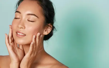 Mannequin asiatique à la peau parfaite, les deux mains posées sur les joues pour apprécier sa peau lisse après l’utilisation de l’Exfoliant Doux Purifiant de la gamme Clear Expert.