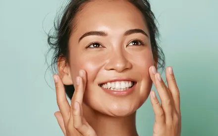 Mannequin asiatique souriante avec une peau parfaite. Elle applique simultanément, avec un doigt sur chaque pommette, le Sérum Purifiant de la gamme Clear Expert.