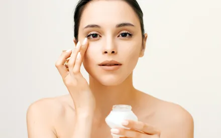 Une femme asiatique au teint frais et lumineux. Elle effectue un massage délicat du bout des doigts juste en dessous de l'œil pour faire pénétrer un sérum contour des yeux.