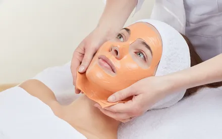 Une femme se fait retirer un masque peel-off anti-âge orange à l'acérola par une spa praticienne.