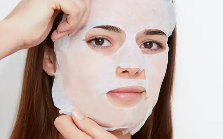 Notre mannequin brune appliquant le masque en tissu Softcell SOS Pureté Hydra+, conçu pour épouser parfaitement l'ensemble du visage.