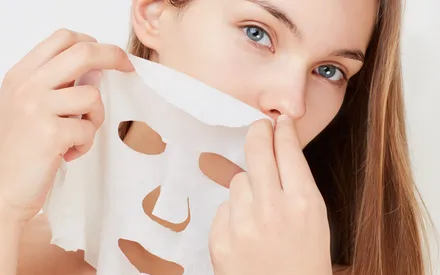 Mannequin en train d'appliquer un masque en tissu sur son visage. Le geste précis illustre un moment de soin à la fois simple et expert.