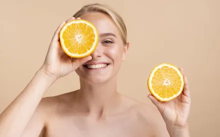 Une femme présente des moitiés d'oranges bio à hauteur de visage, symbolisant la naturalité et l'action coup d'éclat de notre essence à l'eau végétale d'orange.