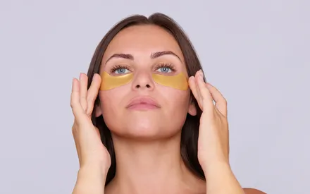 Une mannequin qui tient ses deux patchs hydrogel de couleurs or, comme si elle venait de les appliquer, d'un air sûr d'elle