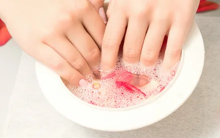Main dans une solution de poudre effervescente mélangée avec de l'eau pour réaliser un soin des ongles et une manucure.